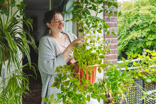 Happy teenage girl with potted tomato plant on balcony