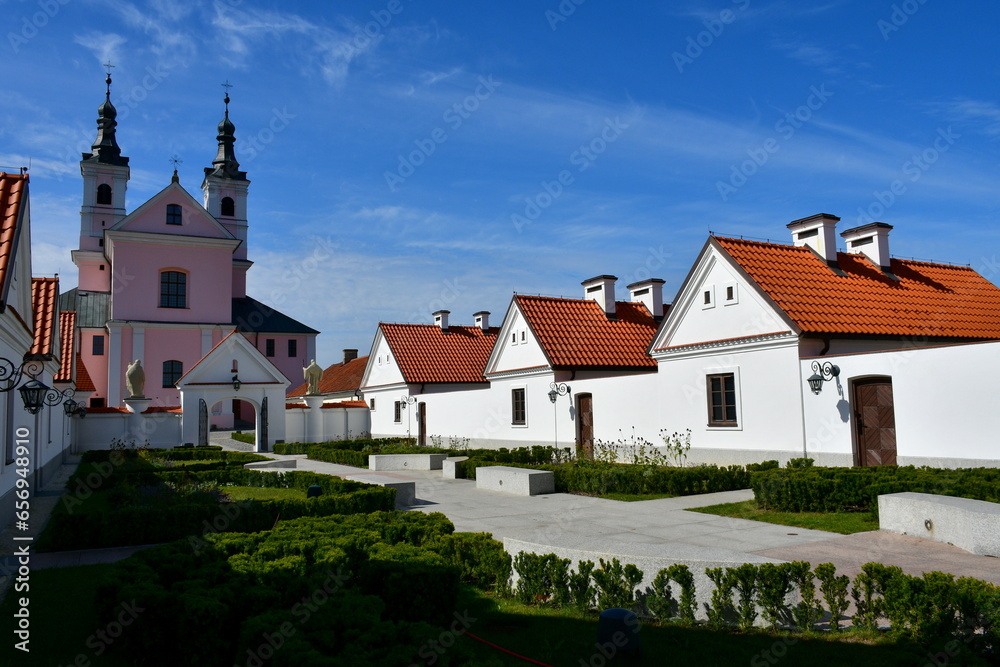 A close up on an old monastery or cloister with numerous houses for monks and priests located next to a big tower seen on a sunny summer day next to a well maintained garden or orchard