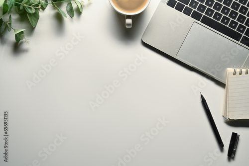White office desk with laptop, cup of coffee, notepad and plant. Top view with space for text