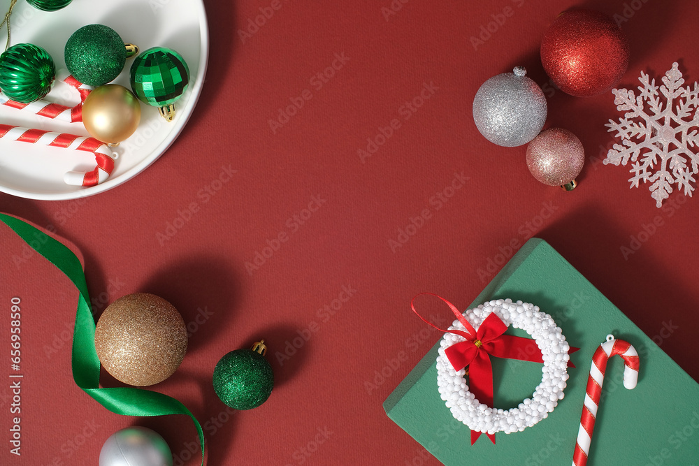 Ideas for decoration on Christmas holiday with cute decorations. Colorful baubles, candy cane, ribbon and gift box arranged on a red background. Top view, scene for advertising with copy space