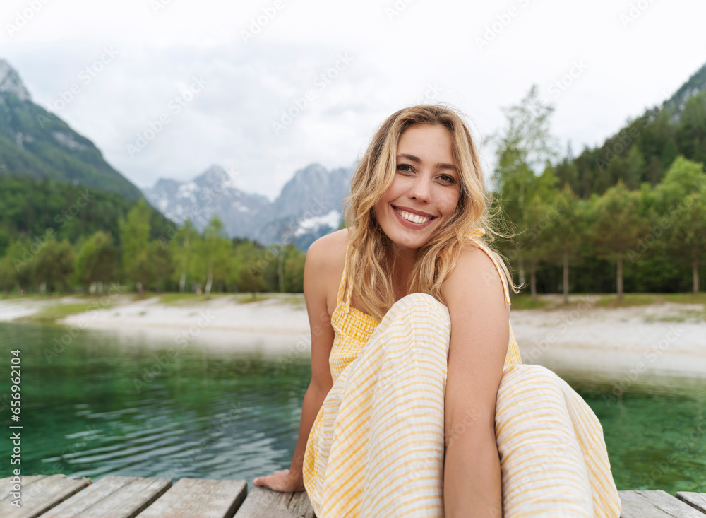 Beautiful smiling woman sitting on pier by river and mountains Beautiful smiling woman sitting on pier by river and mountains