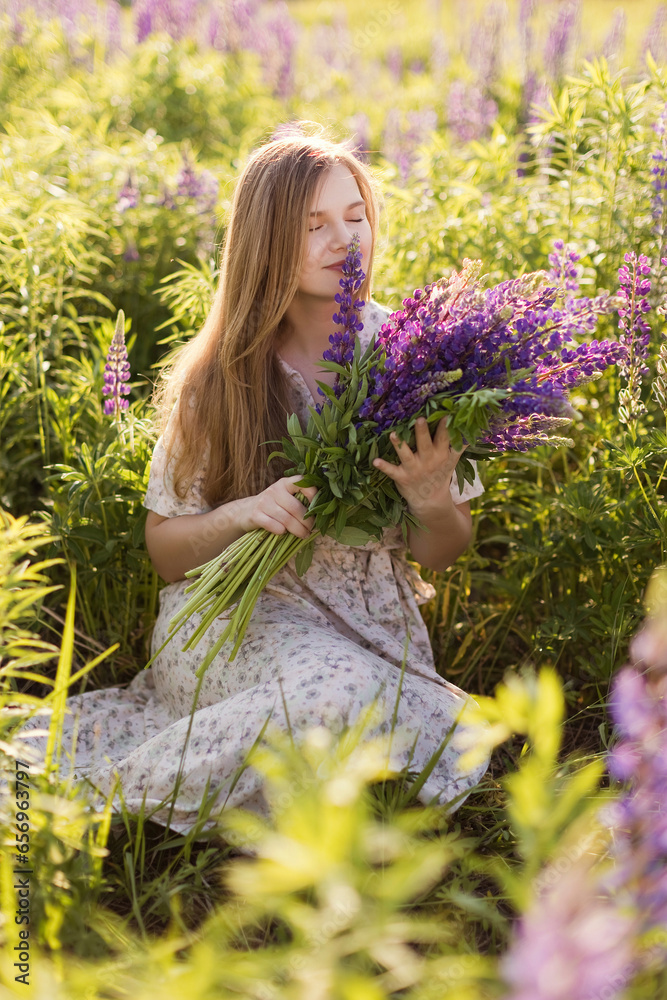 Woman smelling purple lupine flowers sitting in field Woman smelling purple lupine flowers sitting in field