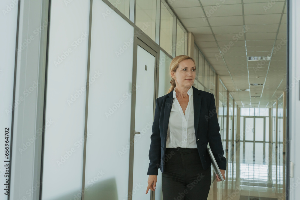 Businesswoman holding laptop and walking in office Businesswoman holding laptop and walking in office