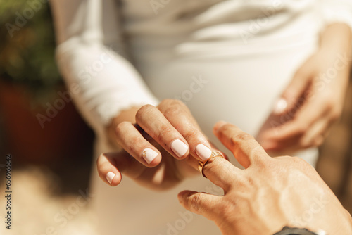 Hand of bride putting wedding ring on groom's finger photo