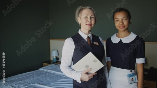 Portrait of female hotel manager and maid standing in room, looking at camera and smilingPortrait of female hotel manager and maid standing in room, looking at camera and smiling photo