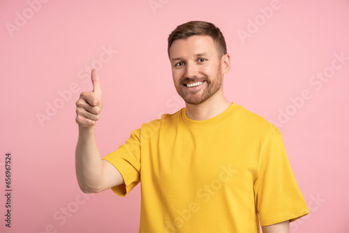 Happy man showing thumb up hand gesture on pink background looking at camera. Banner poster for advertisement, marketing. Positive smiling guy. Like, recommendations, feedback, approval concept. 