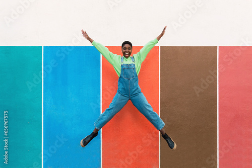 Cheerful young woman jumping in front of multi colored wall photo