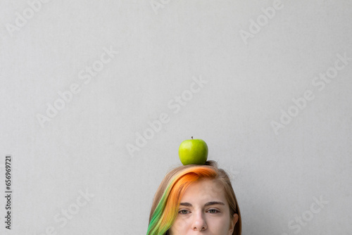 Teenage girl balancing apple on head against gray background photo