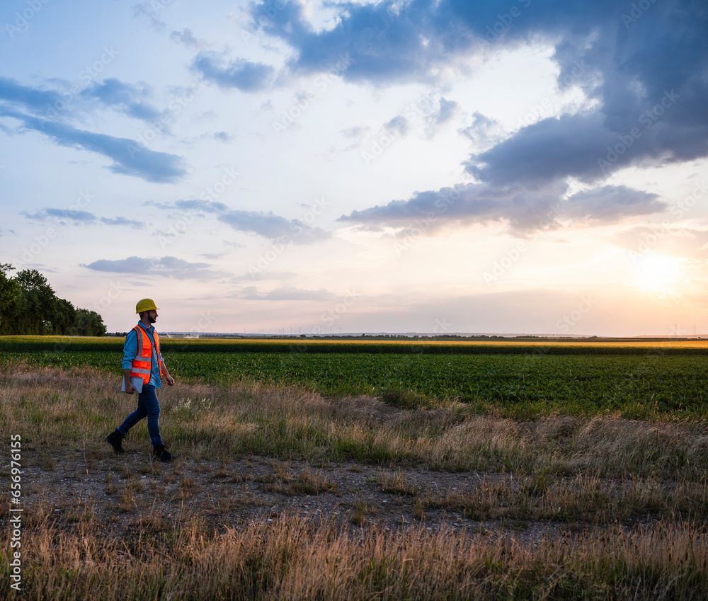 Engineer walking on agricultural field at sunset