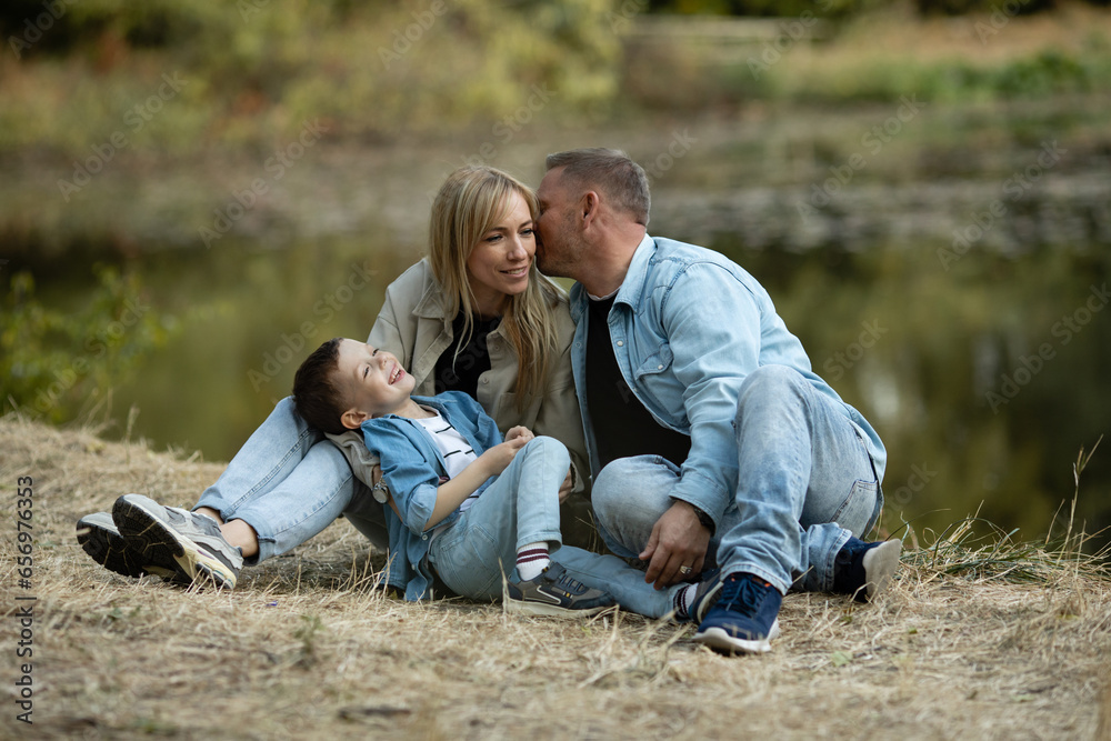 Happy family having fun on the shore of the pond in beautiful golden fall park. Mom, Dad and little child boy having fun near lake or river in autumn. Happy childhood and kid outdoor recreation Happy family having fun on the shore of the pond in beautiful golden fall park. Mom, Dad and little child boy having fun near lake or river in autumn. Happy childhood and kid outdoor recreation