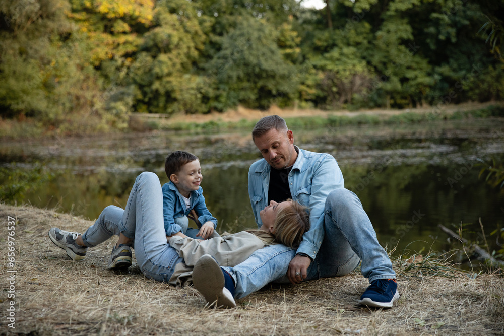 Happy family having fun on the shore of the pond in beautiful golden fall park. Mom, Dad and little child boy having fun near lake or river in autumn. Happy childhood and kid outdoor recreation Happy family having fun on the shore of the pond in beautiful golden fall park. Mom, Dad and little child boy having fun near lake or river in autumn. Happy childhood and kid outdoor recreation