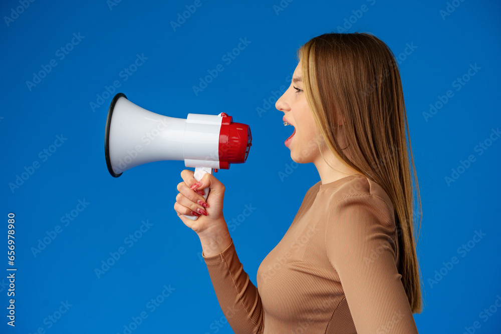 Teen girl making announcement with megaphone on blue background Teen girl making announcement with megaphone on blue background