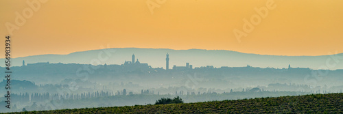 Italy, Tuscany, Siena, Panoramic view of hills and distant city at foggy dawn