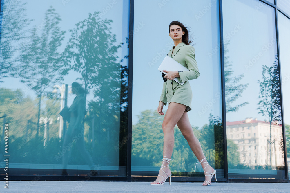 A stylish business lady hurries to the office with a laptop. Urban portrait of a young woman