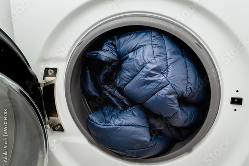 Blue puffer jacket in the drum of open washing machine in laundry room. Washing dirty down jacket in the washer photo
