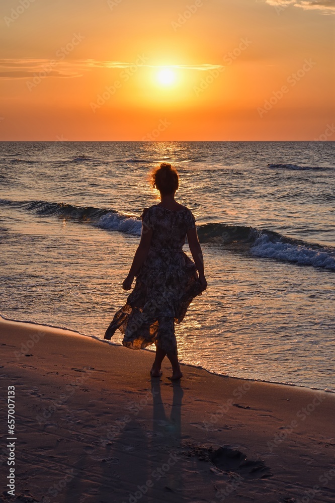 Woman on the seashore in a beautiful evening scenery. Girl walking on the beach with the setting sun in the background. Photo taken at the Baltic Sea in Leba, Poland.