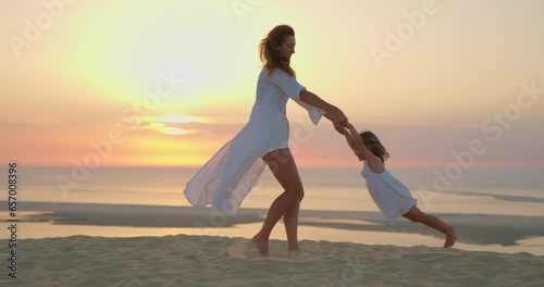 Mother and daughter playing together. Young mother with laughing daughter fooling around at beach during sunset. Young mother having fun while swinging her little girl at sunset