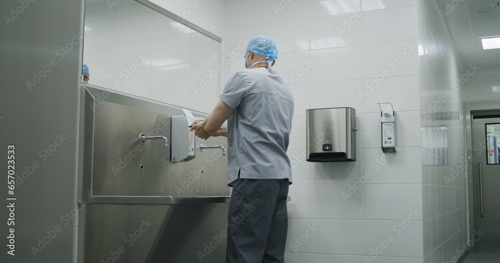 Professional surgeon in uniform washes hands before surgical operation. Paramedic prepares to performing surgery with seriously injured patient. Personnel work in modern medical facility. Slow motion.