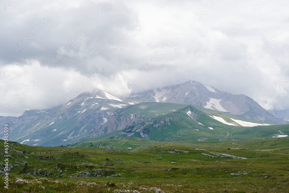 Mountain landscape with clouds and green alpine meadows in the foreground. Mountain landscape with clouds and green alpine meadows in the foreground.
