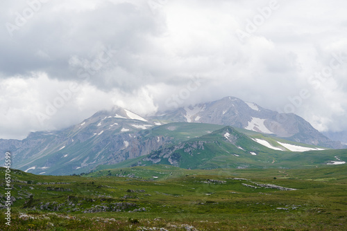 Mountain landscape with clouds and green alpine meadows in the foreground.