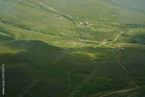 View from above of a tent camp among green alpine meadows.