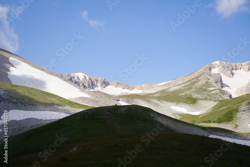 Tiny figures of trekkers walking on top of hill at mountains bottom.