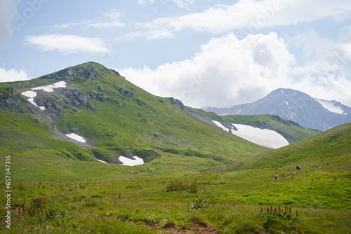 Tourists walk along a mountain route through a green valley.