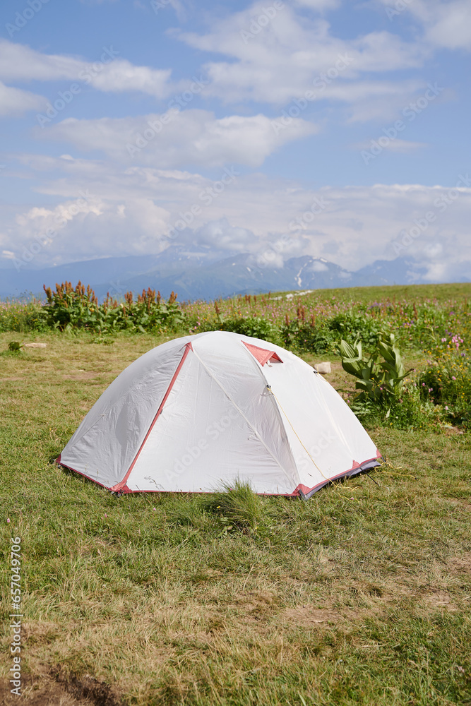 Vertical photo of a white tourist tent against the backdrop of mountains.