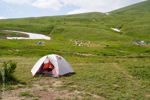 White tourist tent against the backdrop of a campsite among alpine meadows.