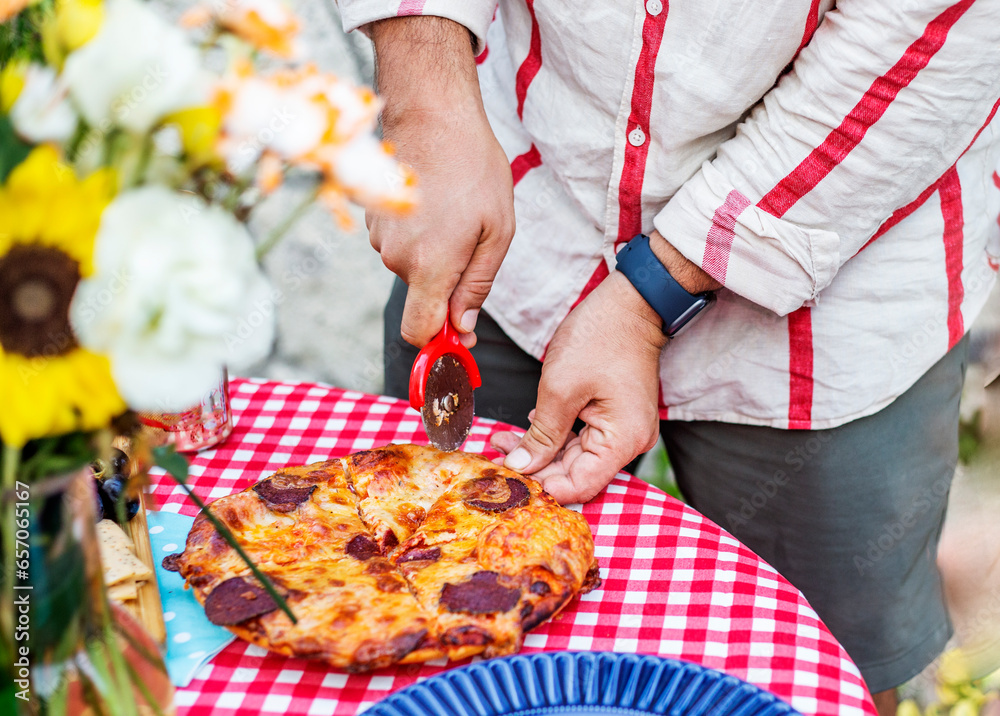 Close-up of a man cutting a slice of pizza with a pizza knife on the table outdoors