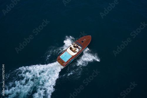 Expensive wooden big boat with people moving on the water aerial view. Boat movement on the water. Motor boat in motion. Luxury wooden big speedboat fast moving on dark water top view.