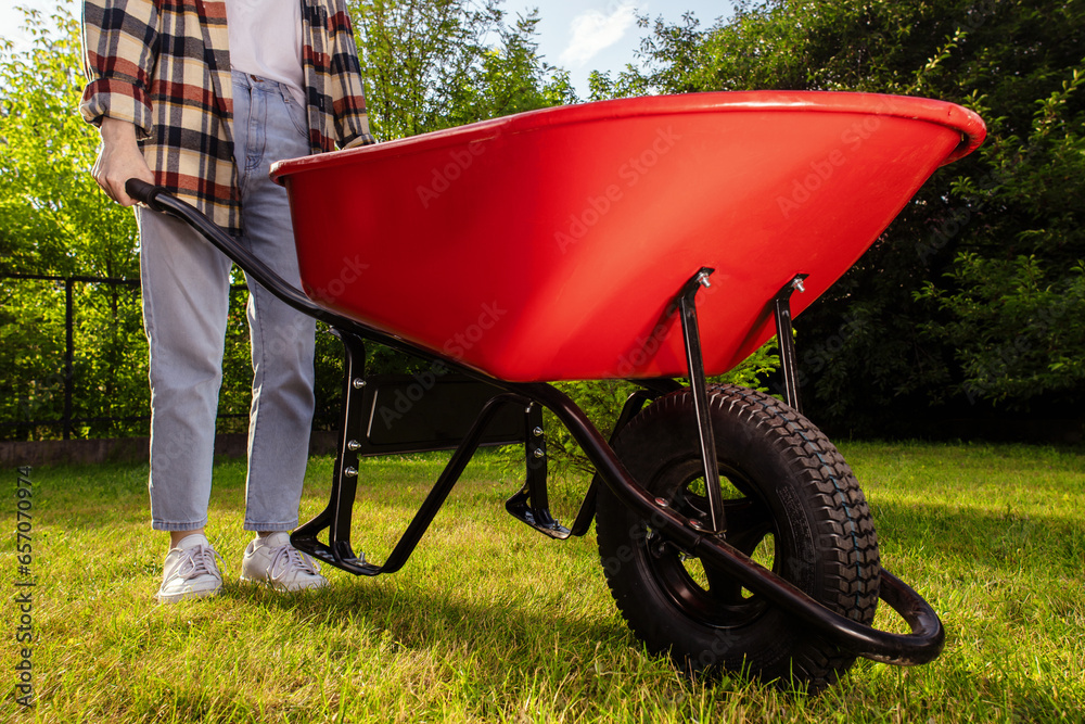 A young gardener with is carrying a metal garden cart through his beautiful green blooming garden. A professional gardener is carrying a wheelbarrow. Sunny autumn day. A young gardener with is carrying a metal garden cart through his beautiful green blooming garden. A professional gardener is carrying a wheelbarrow. Sunny autumn day.