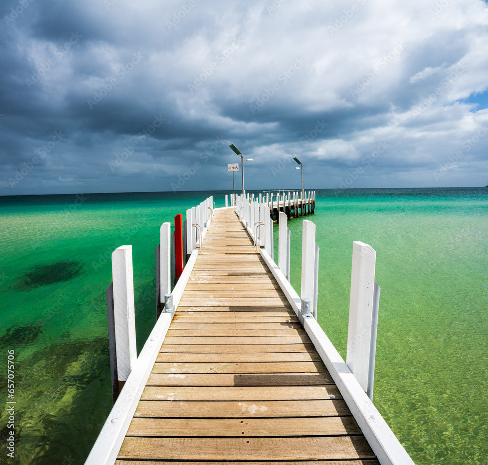 Fototapeta premium Wooden pier with white posts set in turquoise waters and dramatic sky