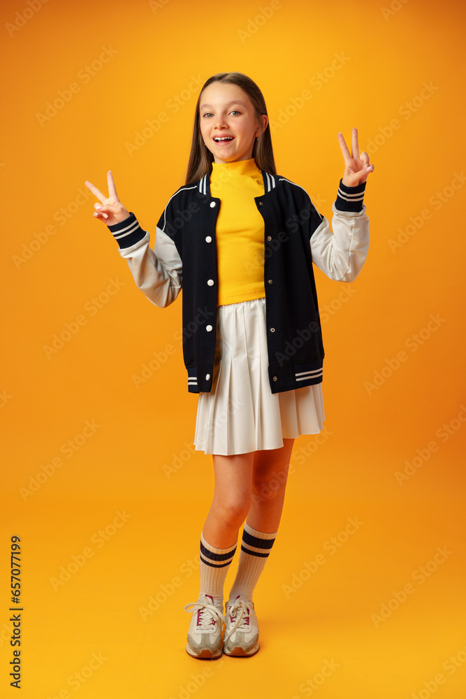 Teen girl makes peace or victory sign over yellow background Teen girl makes peace or victory sign over yellow background