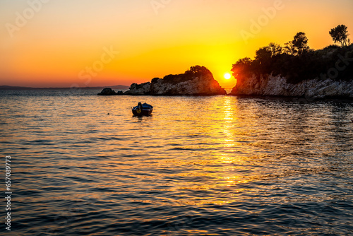 Sunset over the sea. The sun is setting between two rocks in the horizon  with a small motor boat anchored near by