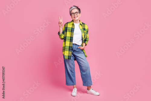 Full length photo of satisfied elderly nice woman wear checkered shirt showing v-sign hand in pocket isolated on pink color background