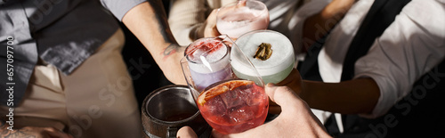 cropped view of multiethnic colleagues clinking glasses with alcohol drinks in cocktail bar, banner