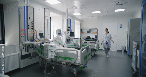 Emergency room with modern equipment in hospital. Elderly man in oxygen mask lies and sleeps in bed after successful surgery. Nurse works on computer in intensive care department of medical facility.