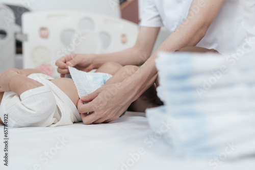 Selective focus hand of mother. Baby lying on bed is changing diaper by his mother. Baby healthcare hygiene concept.