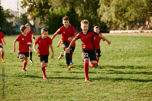 Full length portrait of children's soccer players team running on sport, football field on match in motion. Playing football. © Lustre