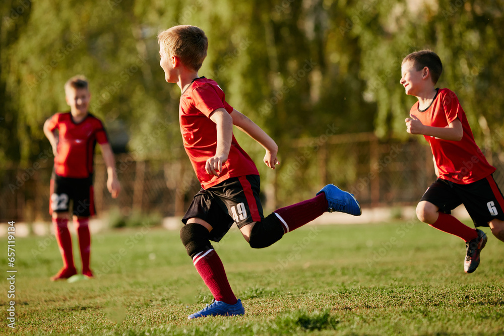 Full length side view portrait of kids, football players in sport uniform training, running at speed in motion before match on soccer field on sunny summer day. Full length side view portrait of kids, football players in sport uniform training, running at speed in motion before match on soccer field on sunny summer day.