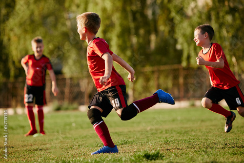 Full length side view portrait of kids, football players in sport uniform training, running at speed in motion before match on soccer field on sunny summer day.