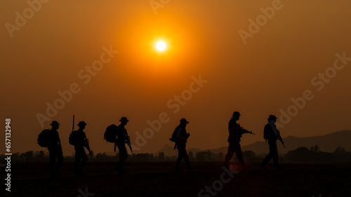 silhouette group of special forces sodiers walking and holding gun over the sunset and colorful orange sky background,