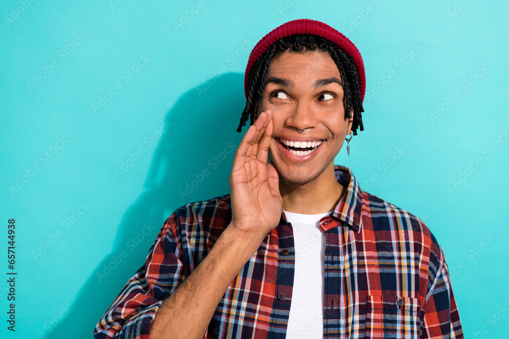 Photo of optimistic cool guy with dreadlocks wear plaid shirt look empty space hand near mouth isolated on turquoise color background
