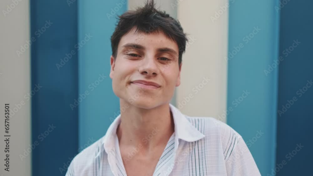 Close up, young smiling man posing looking at camera on striped wall background Close up, young smiling man posing looking at camera on striped wall background