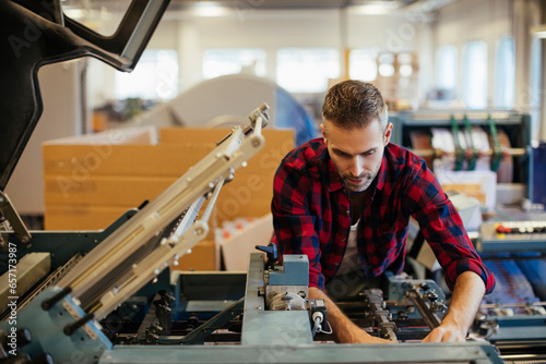 Middle aged Caucasian man fixing a printing press in a printing press office