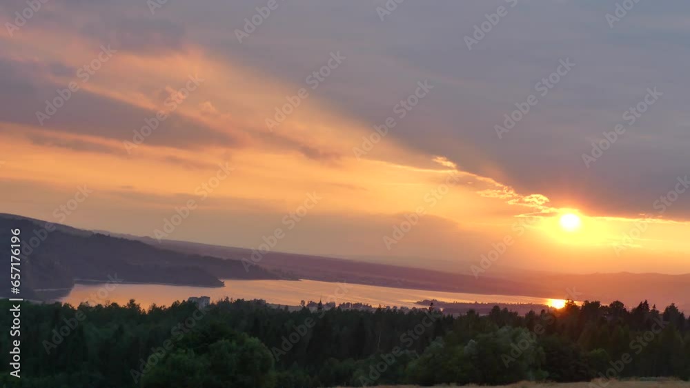Orange yellow evening sky with sunset above Lake Czorsztyn in Poland in Pienin Mountains with green forests. Water in lake illuminated orange by setting sun - real time. Orange yellow evening sky with sunset above Lake Czorsztyn in Poland in Pienin Mountains with green forests. Water in lake illuminated orange by setting sun - real time.