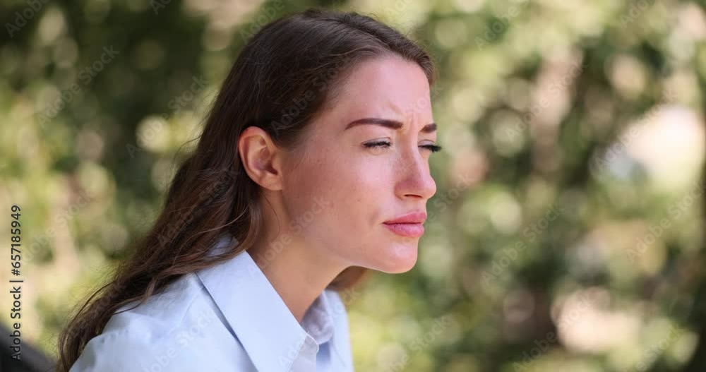 Disappointed woman looks with half-closed eyes against blurred background of green trees. Concept of attentive personality and environment slow motion Disappointed woman looks with half-closed eyes against blurred background of green trees. Concept of attentive personality and environment slow motion