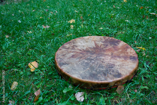 A shaman's tambourine made of genuine leather lies on the green grass.