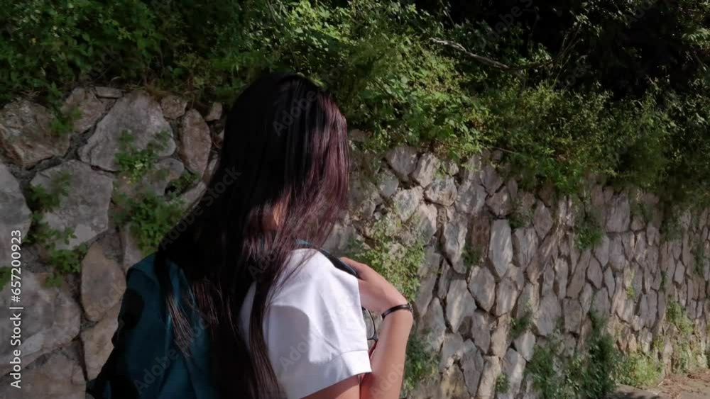 A tourist with a backpack on her shoulder walking down some steps next to an old stone wall in the city of Gaeta A tourist with a backpack on her shoulder walking down some steps next to an old stone wall in the city of Gaeta